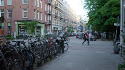Blurred view of amsterdam street with defocused people walking and bicycles lining the sidewalk, capturing the essence of urban life in the netherlands with a dreamy bokeh effect.