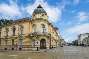 View of classic architecture with a domed tower catches the eye beneath a bright blue sky with fluffy clouds, contrasting with tan and white buildings, Sofia, Sofia City Province, Bulgaria.