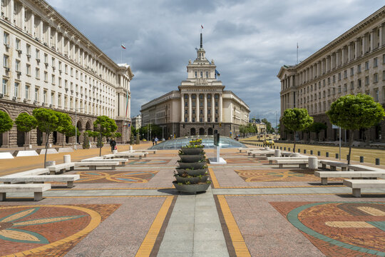 View of geometric patterns on the ground leading to a grand building under a cloudy sky, framed by symmetrical architecture, Sofia, Sofia City Province, Bulgaria.
