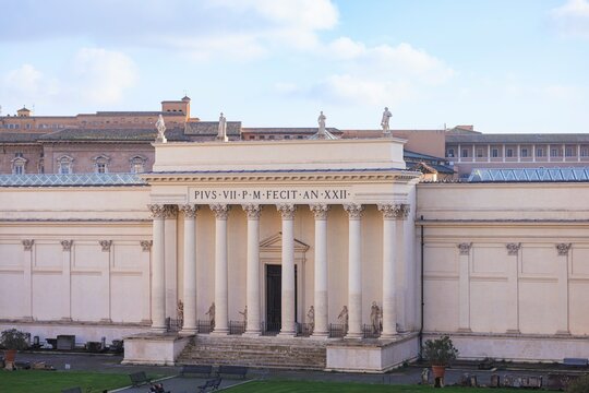 An elegant facade of the Museo Pio Clementino gleams softly in the afternoon light. The stately building is adorned with statues, columns, and intricate stonework