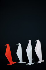 Fototapeta premium Red origami penguin leading a line of white paper penguins: a leadership and difference concept, vertical image