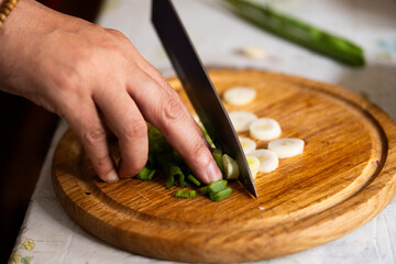 Close-up of a hand using a sharp knife to chop fresh green onions on a wooden board