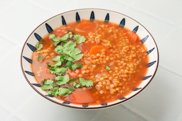 Tasty lentil soup in bowl on white tiled table, closeup