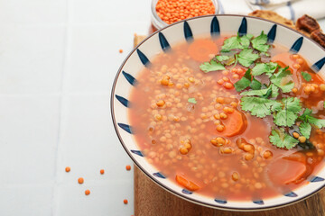 Tasty lentil soup in bowl on white tiled table, closeup. Space for text