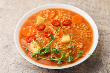 Delicious lentil soup with vegetables in bowl on grey table, closeup