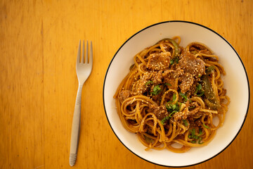 Overhead close-up of savory Beef Chow Mein (or Lo Mein) with green peppers and sesame seeds in a white bowl on a wooden table