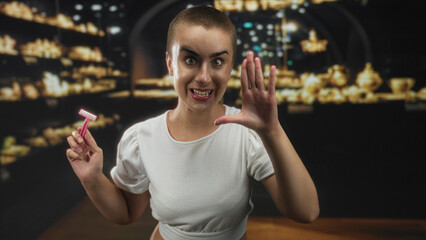 Woman holds a razor in one hand and raises the other hand palm forward inside a display building with lit shelves; self care confidence.