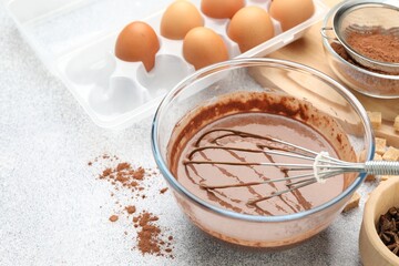 Chocolate dough with whisk in bowl, eggs and spices on grey textured table, closeup