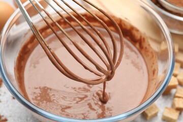 Dripping chocolate dough from whisk into bowl at grey table, closeup