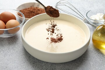 Adding cocoa powder into dough at grey textured table, closeup