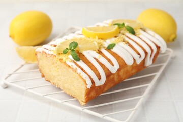 Delicious lemon cake with glaze, fresh fruit slices and mint on light tiled table, closeup