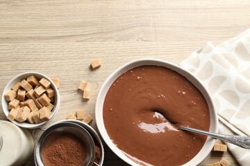 Liquid chocolate dough in bowl, cocoa powder, brown sugar and milk on wooden table, flat lay. Space for text