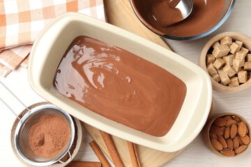 Liquid chocolate dough, cocoa powder, brown sugar, cinnamon and nuts on light wooden table, flat lay
