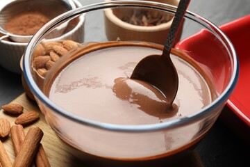 Liquid chocolate dough in bowl, spices, nuts and cocoa powder on table, closeup
