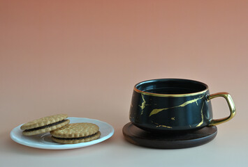 Eine schwarze Tasse Tee im Marmor Design mit Holzuntersetzer und teller mit Prinzenrollen