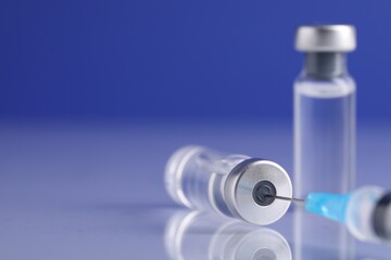 Filling syringe with vaccine from glass vial at light mirror surface against blue background,...