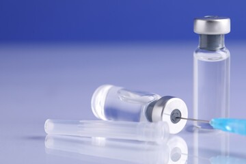 Filling syringe with vaccine from glass vial at light mirror surface against blue background,...
