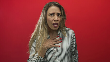 Woman hand on chest in red studio scene wearing striped shirt showing shocked expression; surprise.