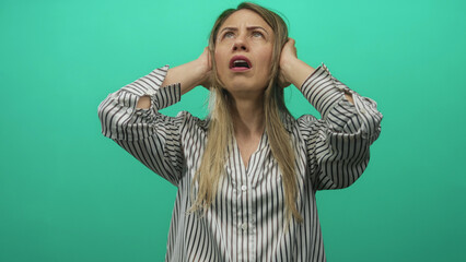 Blonde woman in striped shirt covers ears with hands inside photo studio with pained expression;...