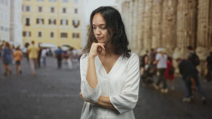 Woman in white dress hand on chin on crowded street near cathedral columns and old building; quiet contemplation.