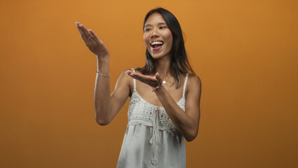 Thai woman wearing white sundress smiles and presents palms up with open hands while tilting head...
