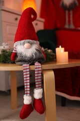 Obraz premium Cute Christmas gnome, burning candles and wreath on wooden table indoors
