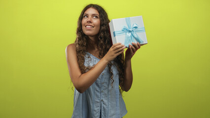 Woman holds a white gift box with blue ribbon and shakes it while listening in a studio; anticipation discovery.