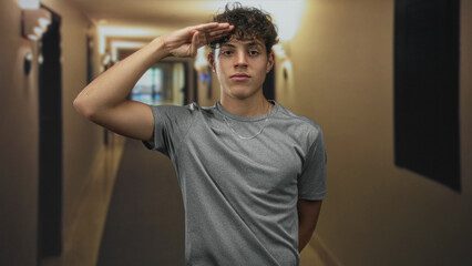 Teenage man salutes with right hand revealing forearm and chain necklace in dim hotel building...