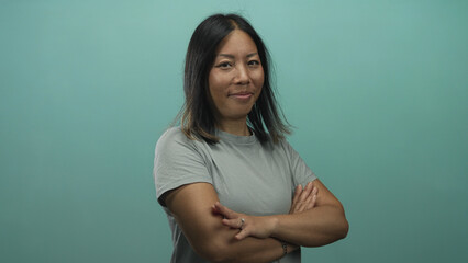 Woman with crossed arms showing ring and bare forearms in studio against teal wall; quiet confidence.