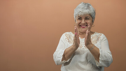 Woman clapping hands in studio wearing white lace blouse and hoop earrings, smiling with raised...