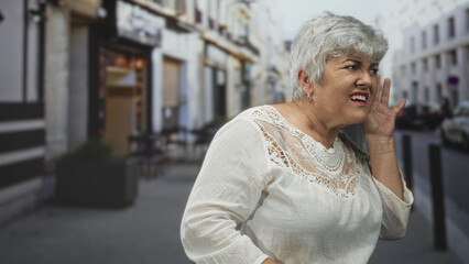 Woman, senior with grey hair and plus size figure, cups ear with hand and squints while trying to...