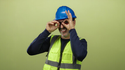 Man wearing blue helmet and yellow vest gestures playfully against green background, showcasing...