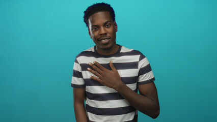 Fototapeta premium Young african american man with hand on chest gesture in teal studio; sincerity trust affirmation hope.