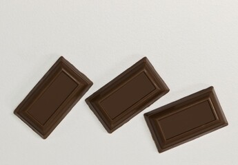 Milk chocolate squares pieces scattered on white background copy space.