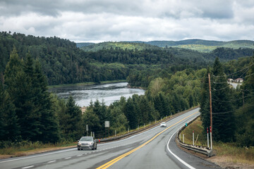 Scenic highway running through a lush green forest with a wide river and rolling hills near La Tuque in Quebec, Canada
