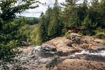 Scenic waterfall flowing over rocky terrain in Parc des Chutes de la Petite Riviere Bostonnais in Quebec, surrounded by lush evergreen forest and natural landscape.