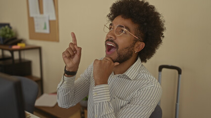 Man in an office with an idea, wearing glasses and a striped shirt, gesturing excitement in a professional indoor setting, conveying creativity and innovation.