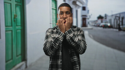 Young man holding a screwdriver to his cheek with hands pressed against his face, looking pensive...