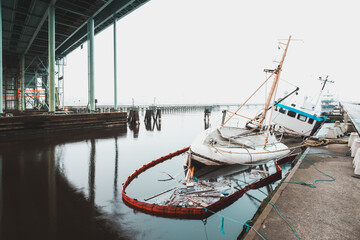 Sunken ship sits under a bridge in Gothenburg with water surrounding it and structures in the background