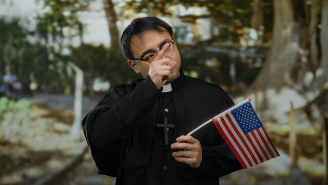 Young man dressed as priest holding american flag in a park setting, blending religious symbolism with national identity in an outdoor environment.
