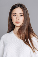 beautiful cute young woman with flawless skin and smooth long hair, soft friendly smile, studio portrait on neutral background, symbolizing natural purity, youthful freshness and skincare care