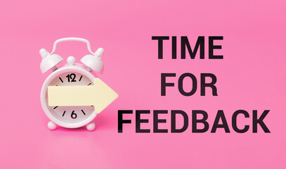 text 'time for feedback' written in black letters, concept of reflection and engaging with your audience or team. White alarm clock with yellow arrow on pink background