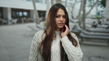 Woman experiencing toothache outdoors in urban setting with long hair and wearing white sweater displaying discomfort on street.