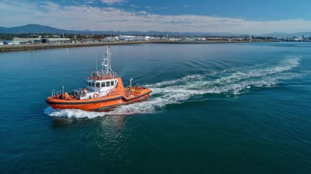 Medium shot captures a pilot boat smoothly steering a vessel through calm waters with clear skies enhancing the peaceful port entry.