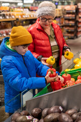 Boy and Elderly Woman Choosing Fresh Bell Peppers at Supermarket Produce Section – Healthy Eating, Family Support and Intergenerational Interaction. Grandmother and Grandson Selecting Fresh Peppers 