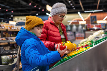 Boy and Elderly Woman Choosing Fresh Bell Peppers at Supermarket Produce Section – Healthy Eating, Family Support and Intergenerational Interaction. Grandmother and Grandson Selecting Fresh Peppers