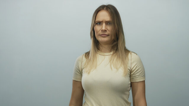 Young blonde woman standing against an isolated white background with a thoughtful expression in a studio setting.