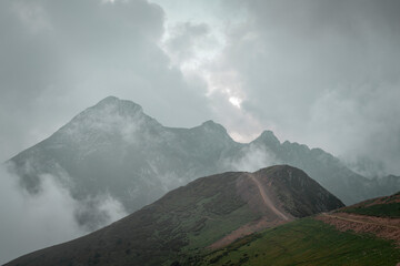 Mist surrounds mountain peaks with clouds overhead during a cloudy day in a remote area