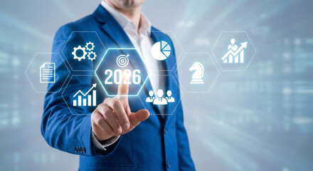 A businessman in a blue suit interacting with a futuristic digital interface displaying business goals and strategic icons for the year 2026.