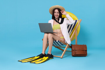 Businesswoman with laptop and flippers in deck chair on light blue background © New Africa